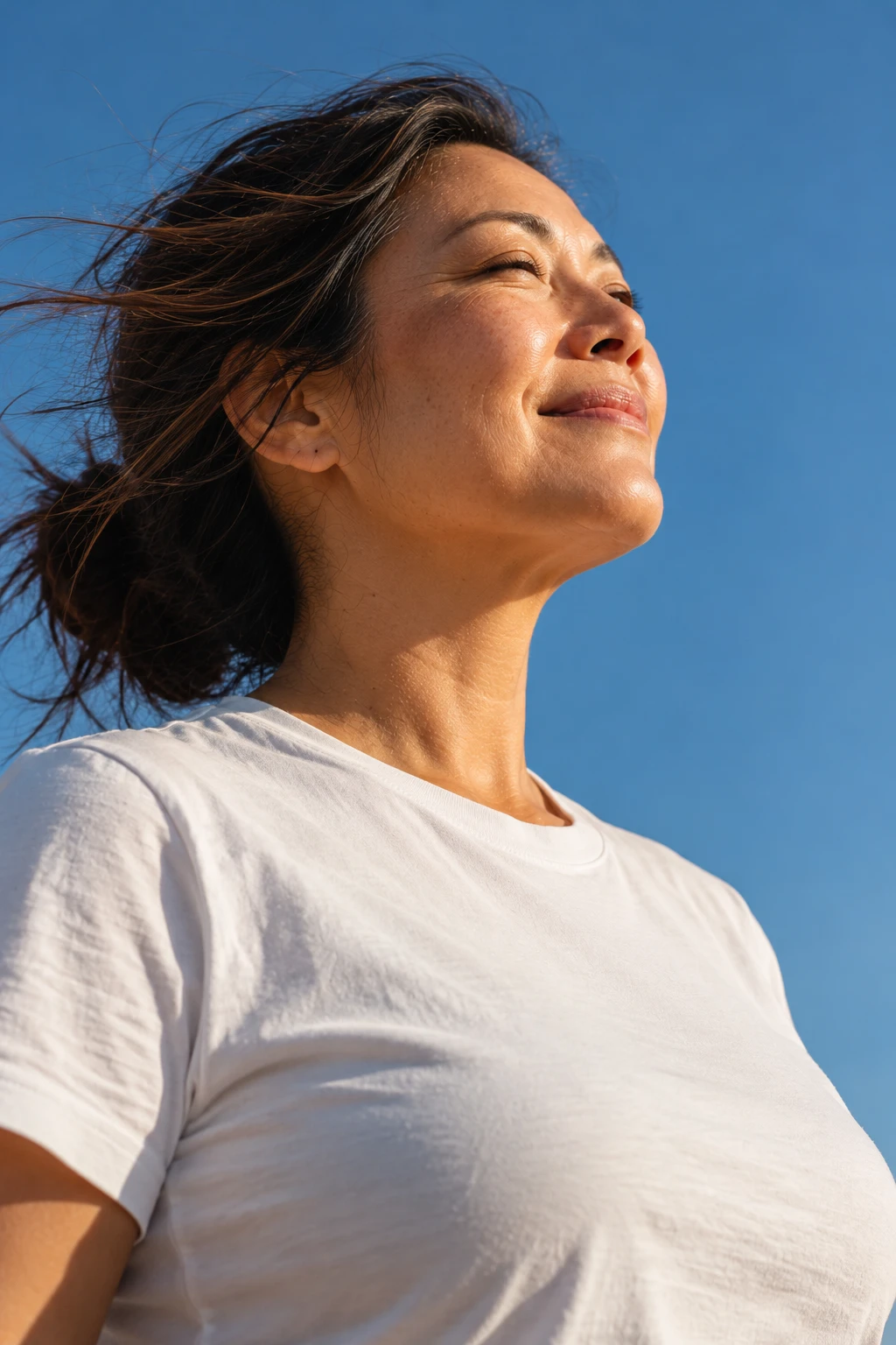 Woman smiling with her eyes closed under a blue sky